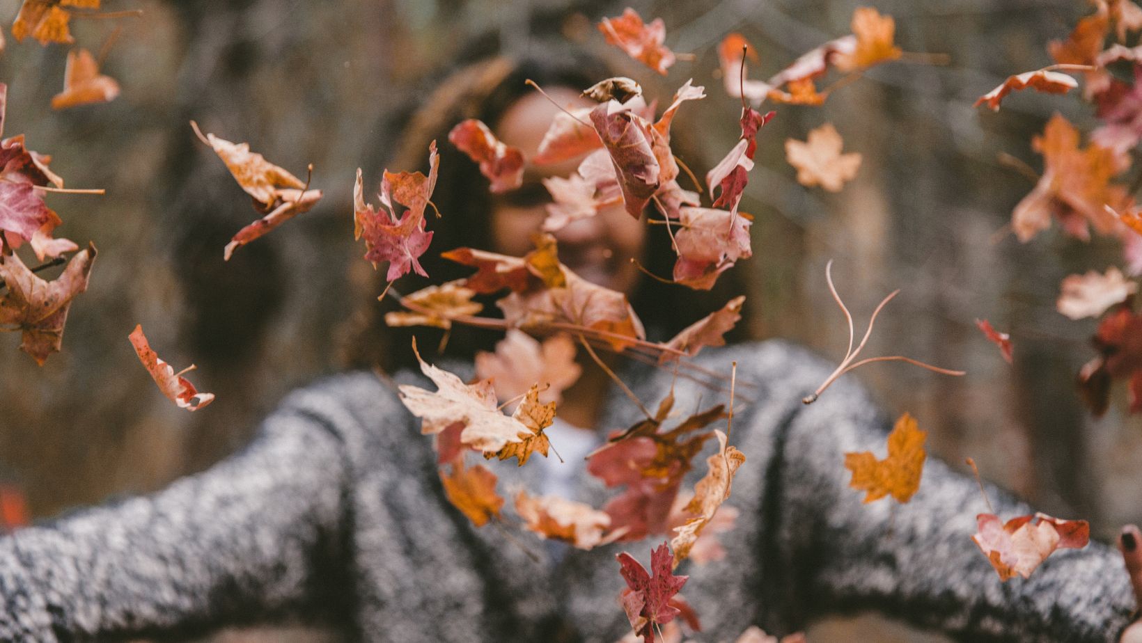 Blurred image of woman throwing autumn leaves into the air